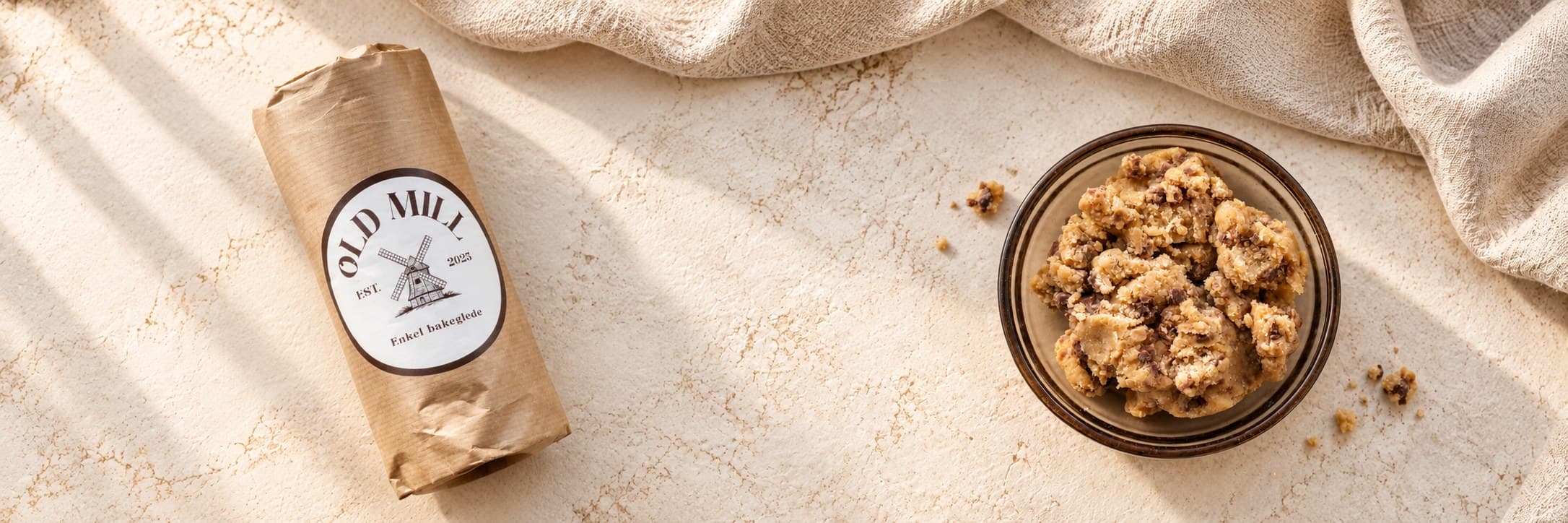 Old Mill cookie dough pakket i brunt papir med etikett, ved siden av en glassbolle med deig